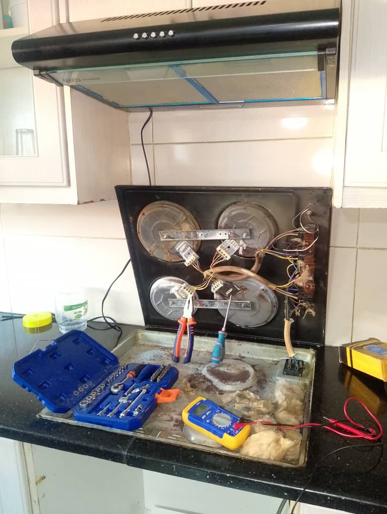 Ceramic hob opened on a kitchen counter with tools and a multimeter during a stove repair
