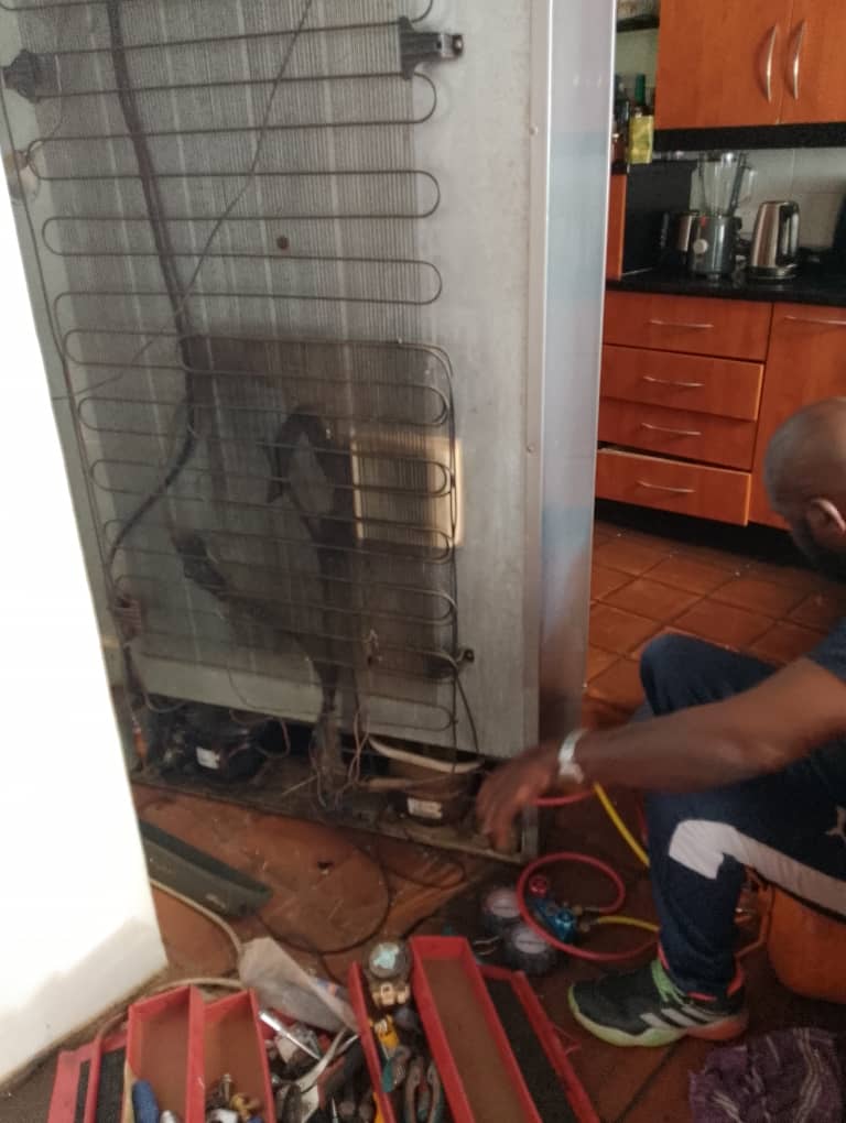 Technician working at the back of a fridge beside its condenser coil