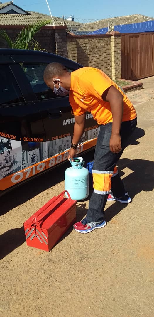 Technician with refrigerant cylinders and a toolbox beside the service vehicle