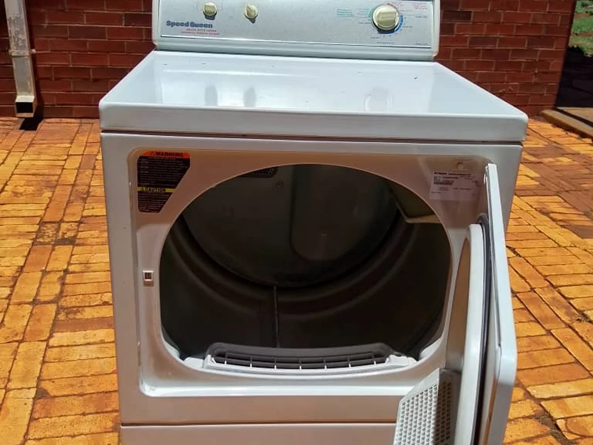 White tumble dryer with its door open on a brick patio