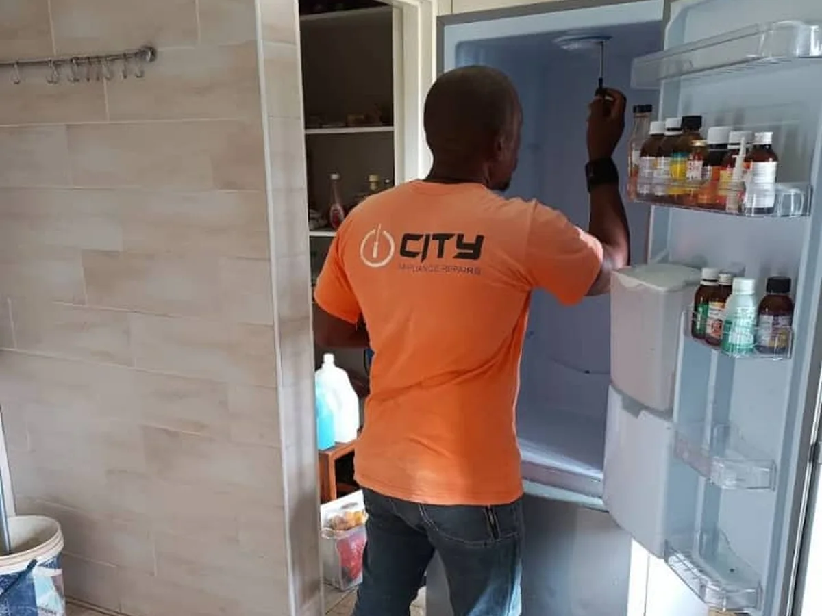 City Appliance Repairs technician working on an open fridge in a customer’s kitchen