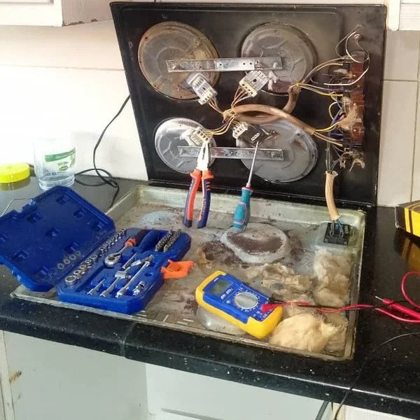 Ceramic hob opened on a kitchen counter with tools and a multimeter during a repair